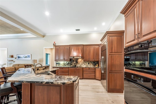 kitchen featuring a breakfast bar area, dobule oven black, a sink, custom exhaust hood, and backsplash