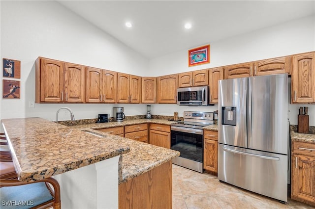 kitchen featuring a peninsula, light stone countertops, a kitchen bar, and stainless steel appliances