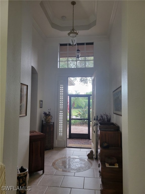 foyer featuring a raised ceiling, light tile patterned floors, ornamental molding, and a towering ceiling