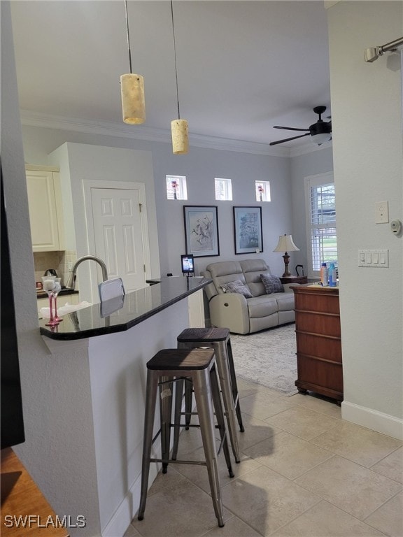 kitchen with kitchen peninsula, ceiling fan, crown molding, hanging light fixtures, and a breakfast bar area