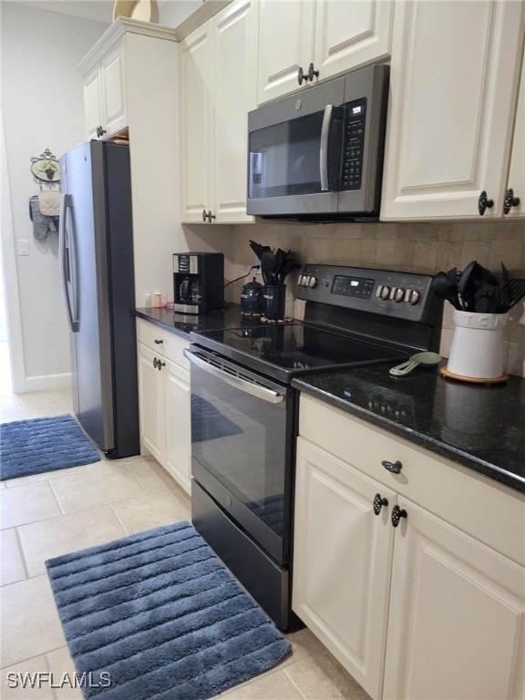 kitchen featuring white cabinets, light tile patterned floors, stainless steel appliances, and dark stone counters