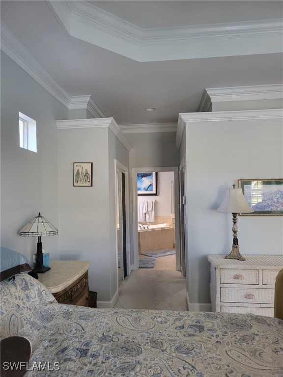 bedroom with light carpet, connected bathroom, a raised ceiling, and crown molding