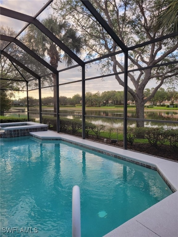 pool at dusk with glass enclosure, a water view, and an in ground hot tub