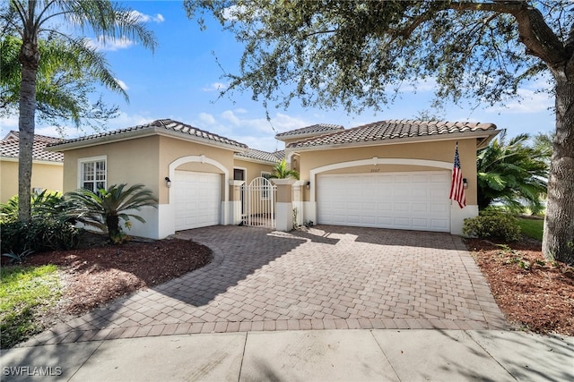 mediterranean / spanish home featuring decorative driveway, a gate, a tile roof, and stucco siding