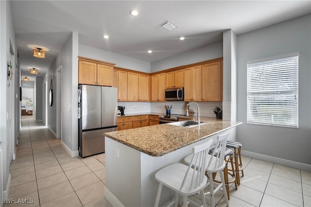 kitchen featuring light stone counters, a peninsula, a breakfast bar, a sink, and appliances with stainless steel finishes