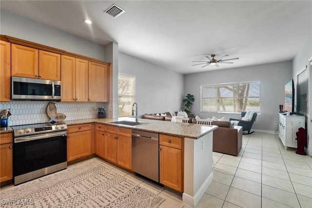 kitchen with light tile patterned floors, stainless steel appliances, a peninsula, a sink, and open floor plan