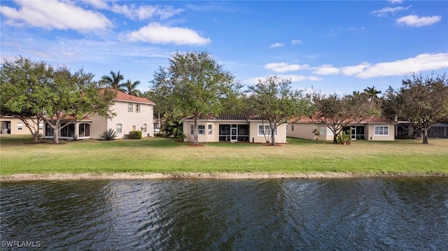 rear view of house with a water view, a lawn, and stucco siding