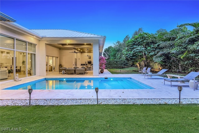 pool at dusk featuring ceiling fan, an outdoor hangout area, a patio, and a yard