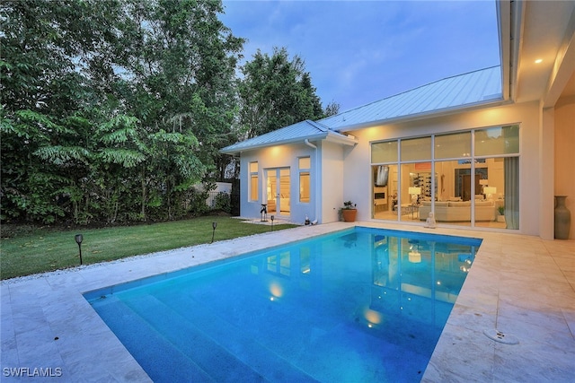 pool at dusk with a yard and a patio