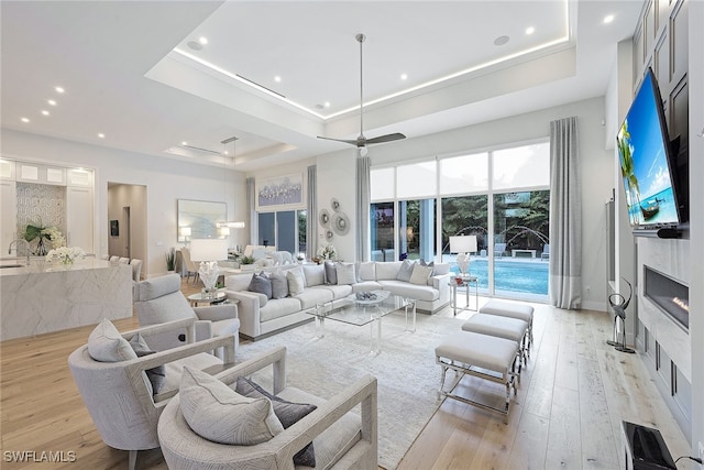 living room featuring a raised ceiling, ceiling fan, a premium fireplace, and light wood-type flooring