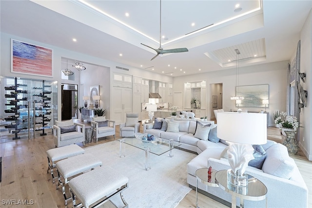 living room featuring a tray ceiling, ceiling fan, and light hardwood / wood-style flooring