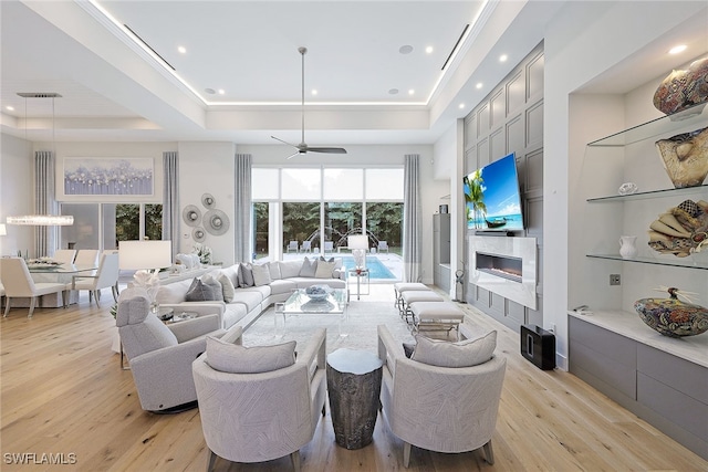 living room with ceiling fan, light hardwood / wood-style floors, and a tray ceiling