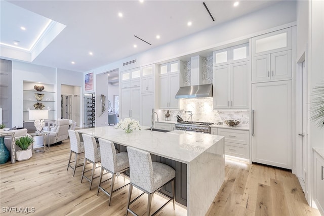 kitchen with sink, an island with sink, light hardwood / wood-style floors, a kitchen bar, and white cabinets