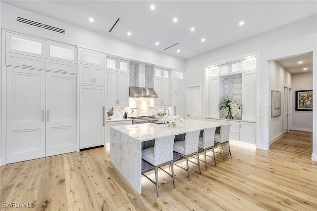 kitchen with white cabinetry, a kitchen island with sink, a kitchen bar, and light wood-type flooring