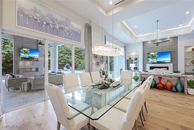 dining space featuring ceiling fan with notable chandelier, a raised ceiling, light wood-type flooring, and built in shelves