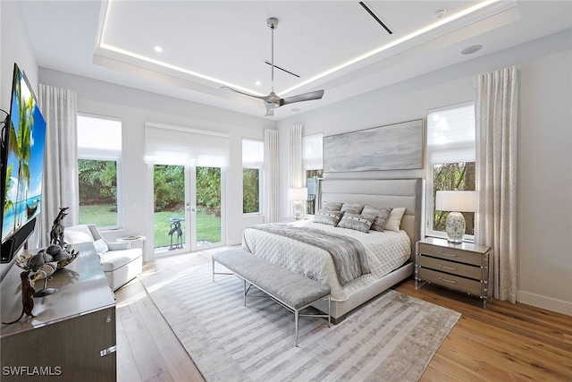 bedroom with ceiling fan, a raised ceiling, light wood-type flooring, and french doors