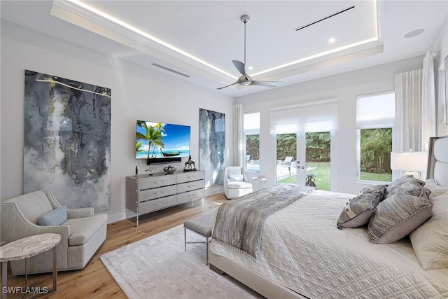 bedroom with a raised ceiling, ceiling fan, french doors, and light wood-type flooring