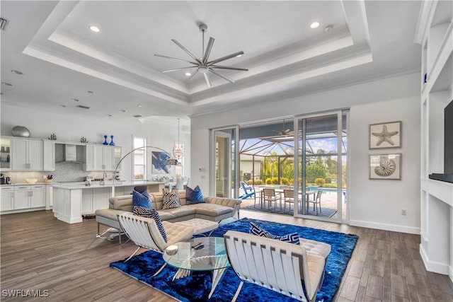 living room with a tray ceiling, crown molding, a healthy amount of sunlight, and dark hardwood / wood-style floors