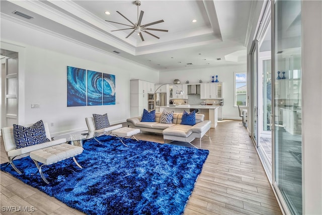 living room featuring light wood-type flooring, a raised ceiling, ceiling fan, and ornamental molding