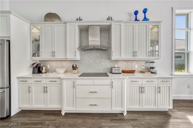 kitchen featuring white cabinetry, stainless steel refrigerator, a healthy amount of sunlight, and wall chimney range hood