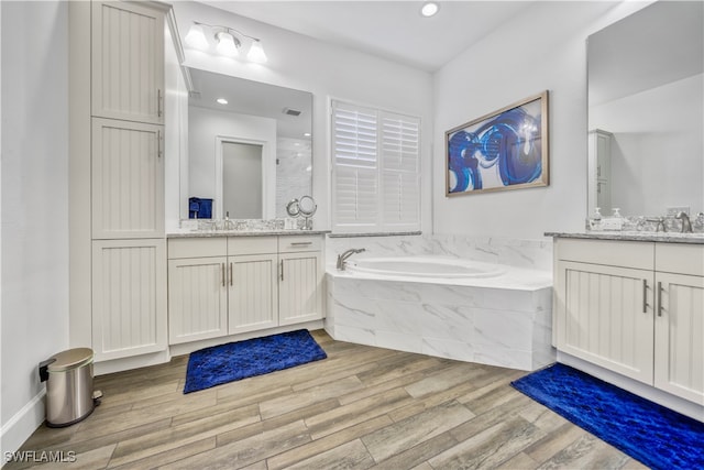 bathroom with a relaxing tiled tub, wood-type flooring, and vanity