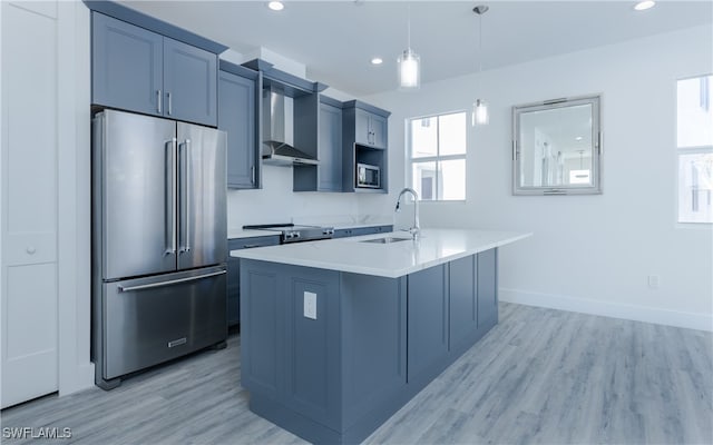 kitchen featuring stainless steel appliances, a kitchen island with sink, wall chimney range hood, sink, and pendant lighting