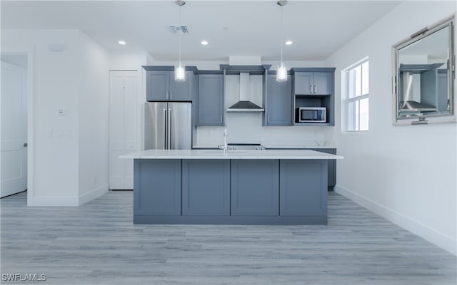 kitchen featuring a kitchen island with sink, sink, hanging light fixtures, wall chimney exhaust hood, and appliances with stainless steel finishes