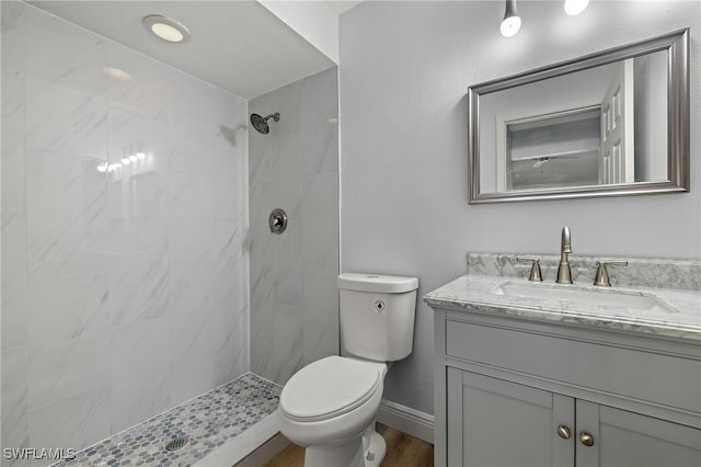 bathroom with hardwood / wood-style flooring, vanity, toilet, and tiled shower