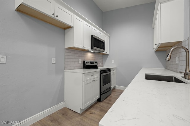 kitchen featuring appliances with stainless steel finishes, backsplash, sink, light hardwood / wood-style flooring, and white cabinetry