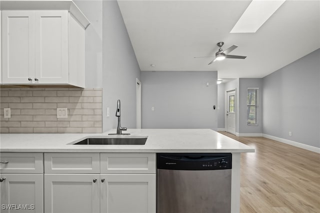 kitchen with dishwasher, sink, a skylight, light wood-type flooring, and white cabinetry