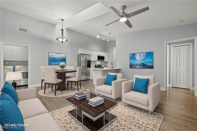 living room featuring vaulted ceiling, ceiling fan, sink, light hardwood / wood-style flooring, and washing machine and dryer