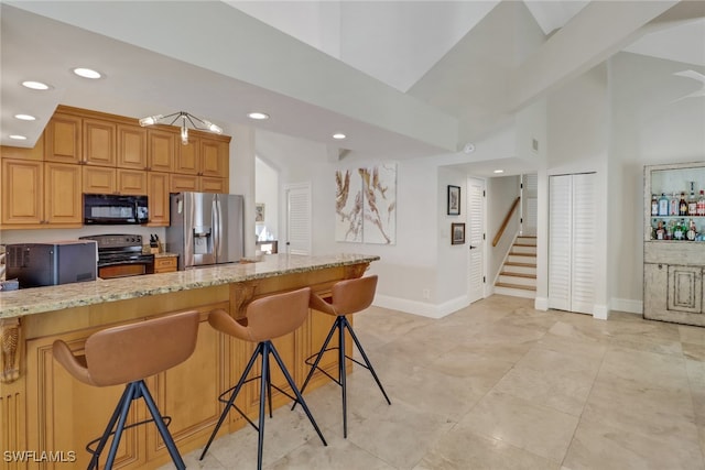 kitchen with light tile patterned floors, light stone countertops, appliances with stainless steel finishes, a towering ceiling, and a breakfast bar area