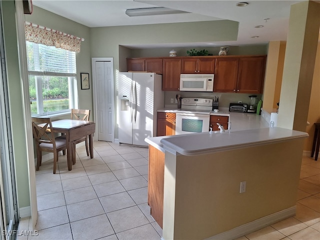 kitchen featuring kitchen peninsula, light tile patterned floors, and white appliances