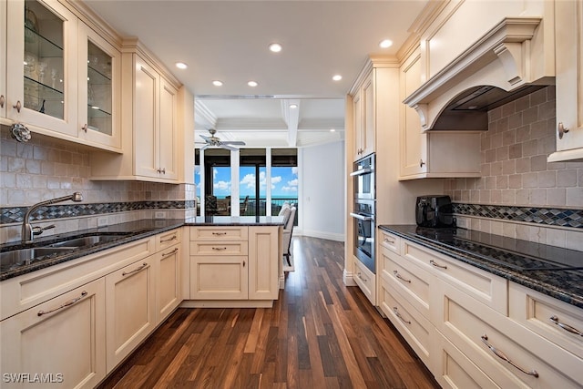 kitchen with sink, dark wood-type flooring, cream cabinets, dark stone counters, and custom range hood