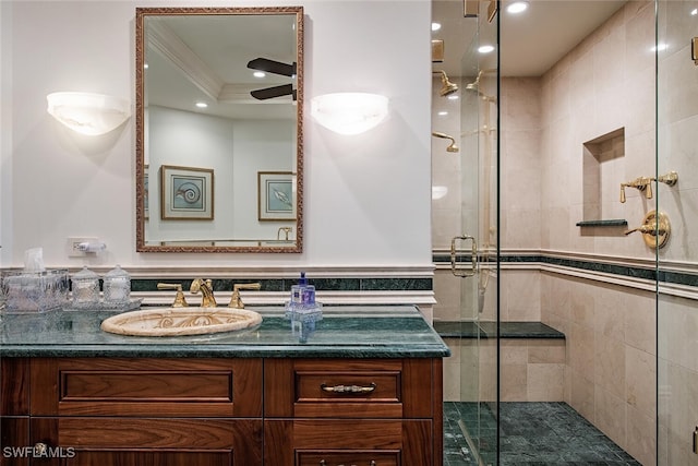 bathroom with vanity, a shower with door, ceiling fan, ornamental molding, and tile walls
