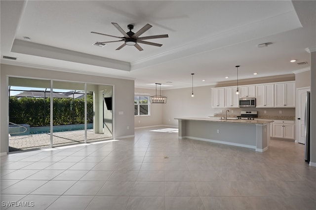 kitchen with a kitchen island with sink, white cabinets, hanging light fixtures, appliances with stainless steel finishes, and a tray ceiling