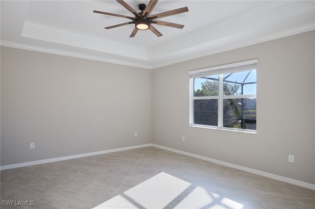 tiled empty room with ceiling fan, a raised ceiling, and ornamental molding