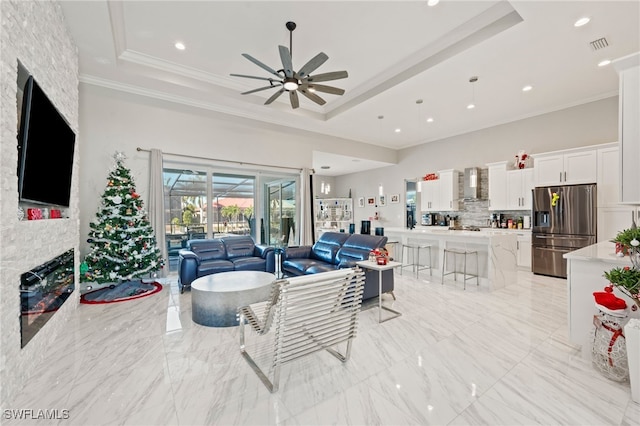 living room with a tray ceiling, ceiling fan, a fireplace, and crown molding