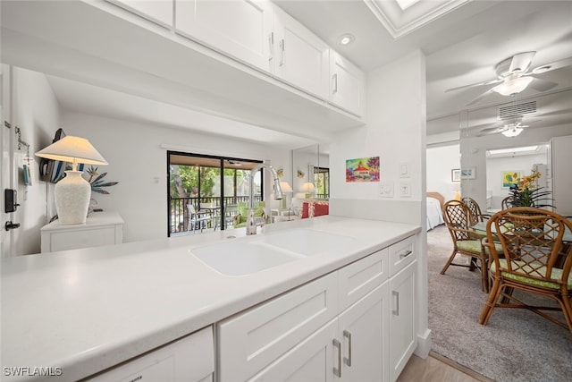 kitchen with kitchen peninsula, light wood-type flooring, ceiling fan, sink, and white cabinetry