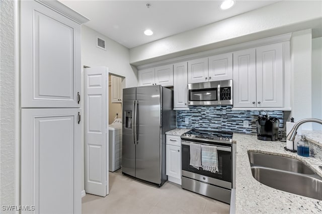 kitchen with light stone countertops, stainless steel appliances, sink, light tile patterned floors, and white cabinets