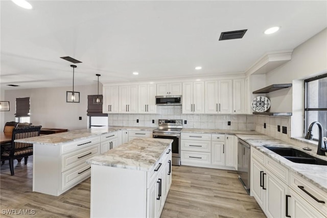 kitchen with light stone counters, hanging light fixtures, a center island, stainless steel appliances, and sink