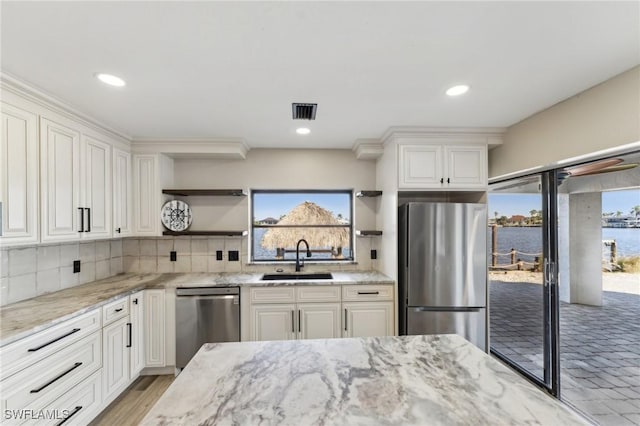 kitchen featuring stainless steel appliances, white cabinets, sink, and a water view