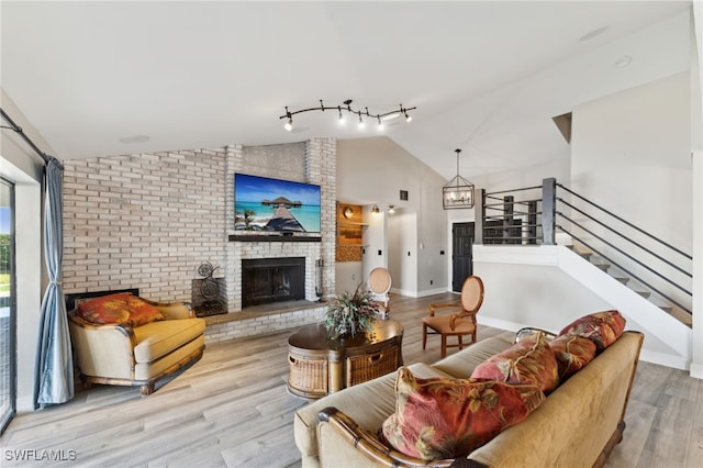 living room featuring lofted ceiling, a brick fireplace, light hardwood / wood-style floors, and a notable chandelier