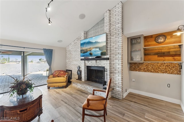 living room with vaulted ceiling, a brick fireplace, and light hardwood / wood-style floors