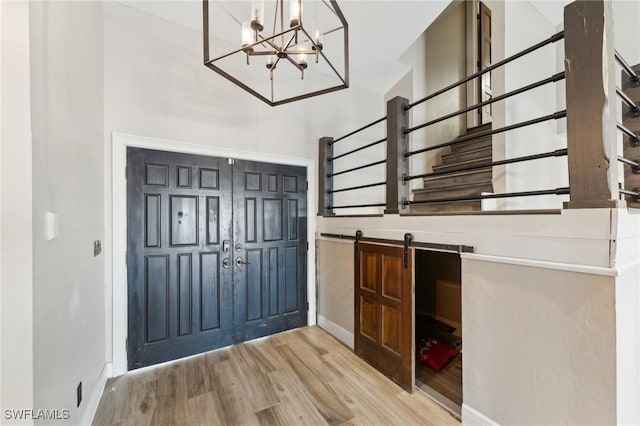 foyer with light hardwood / wood-style floors, a notable chandelier, a towering ceiling, and a barn door