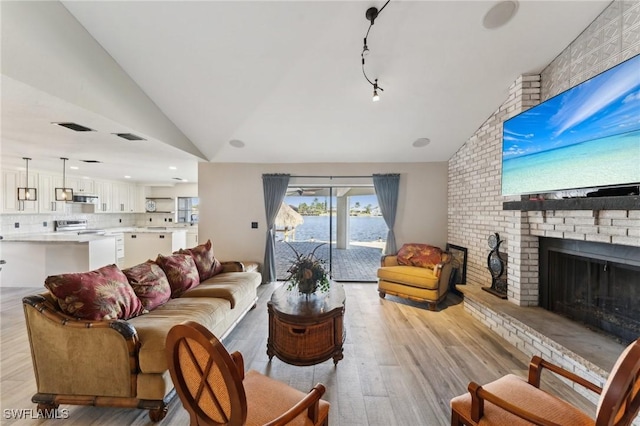 living room featuring lofted ceiling, a brick fireplace, and light wood-type flooring