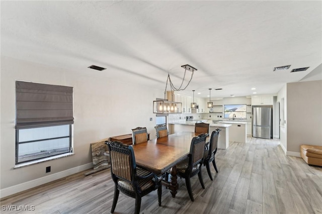 dining area with sink, a chandelier, and light wood-type flooring