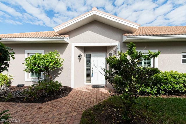 doorway to property with a patio area, a tile roof, and stucco siding