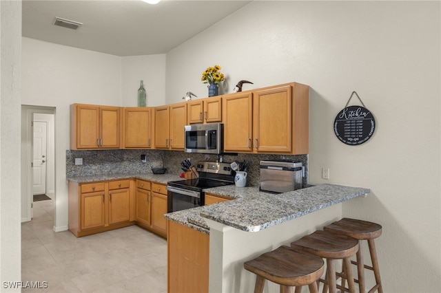 kitchen featuring light stone counters, a towering ceiling, visible vents, appliances with stainless steel finishes, and tasteful backsplash