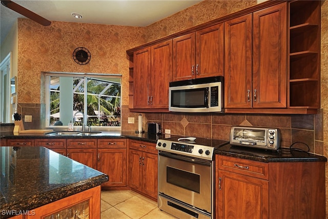 kitchen with appliances with stainless steel finishes, light tile patterned floors, dark stone counters, and sink